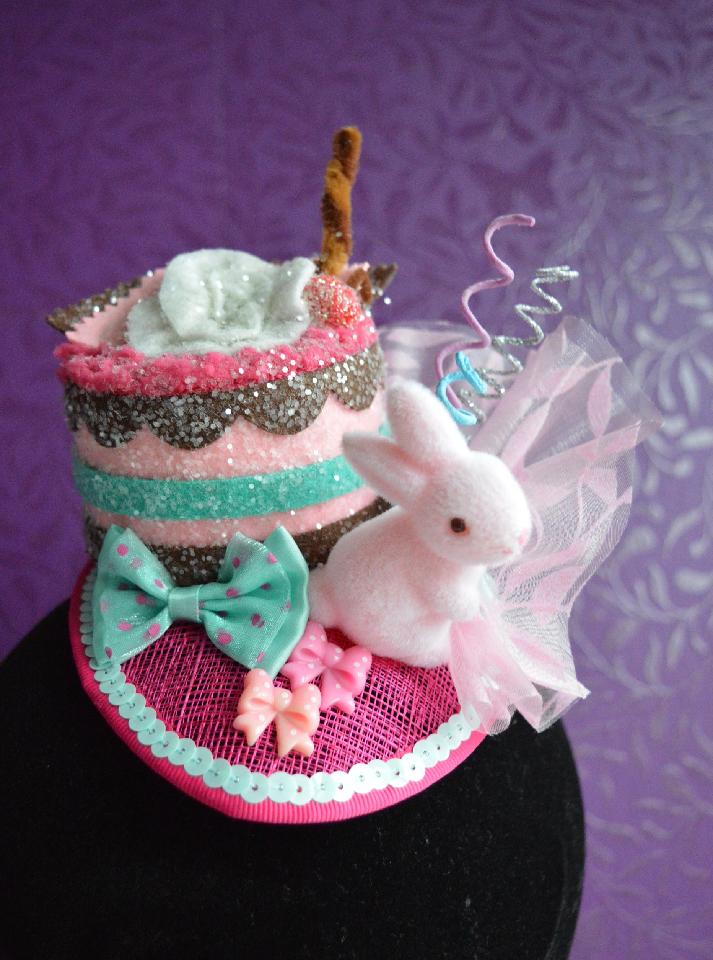IMAGE - Pink sinamay fascinator with glittered cake and pink bunny. Decorated with pink organza, curly sticks and bows. Fixes to the hair with a comb.