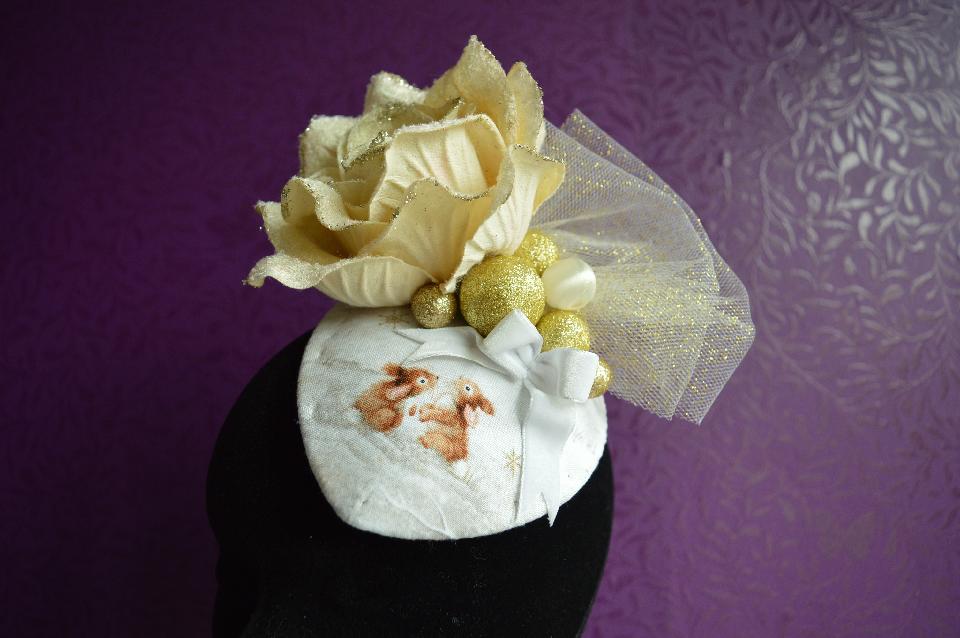 IMAGE - Fabric covered fascinator with gold rose, glittered tulle, gold and cream spheres and white velvet bow. Two bunnies are printed on the fabric. Fixes to hair with a comb.