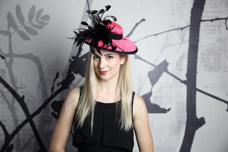IMAGE - Handblocked hot pink sinamay hat. Brim is finished with black ribbon, on the side is a cluster of black feathers. Stays on with an elastic.
