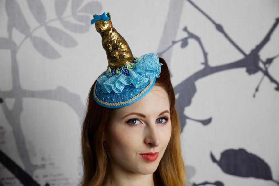 IMAGE - Blue sinamay fascinator with gold cat and blue lace. Decorated with green and blue porcelain roses and glass beads. Finished with gold trim. Fixes to hair with a comb.