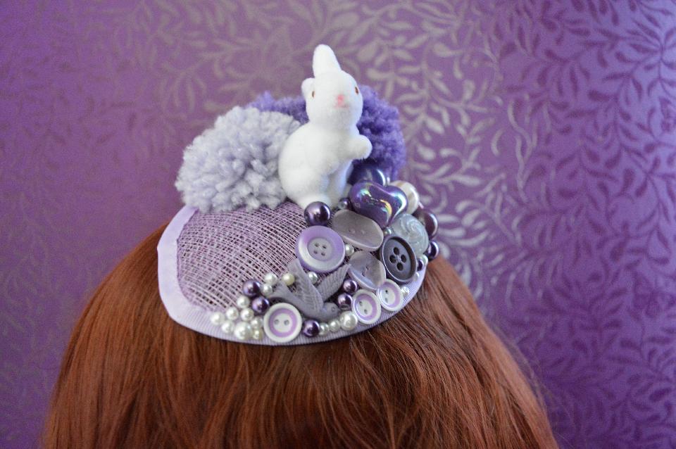 IMAGE - Lilac drop-shaped sinamey fascinator with purple ponpons and white bunny. Decorated with purple buttons and pearls. Fixes to hair with a comb.