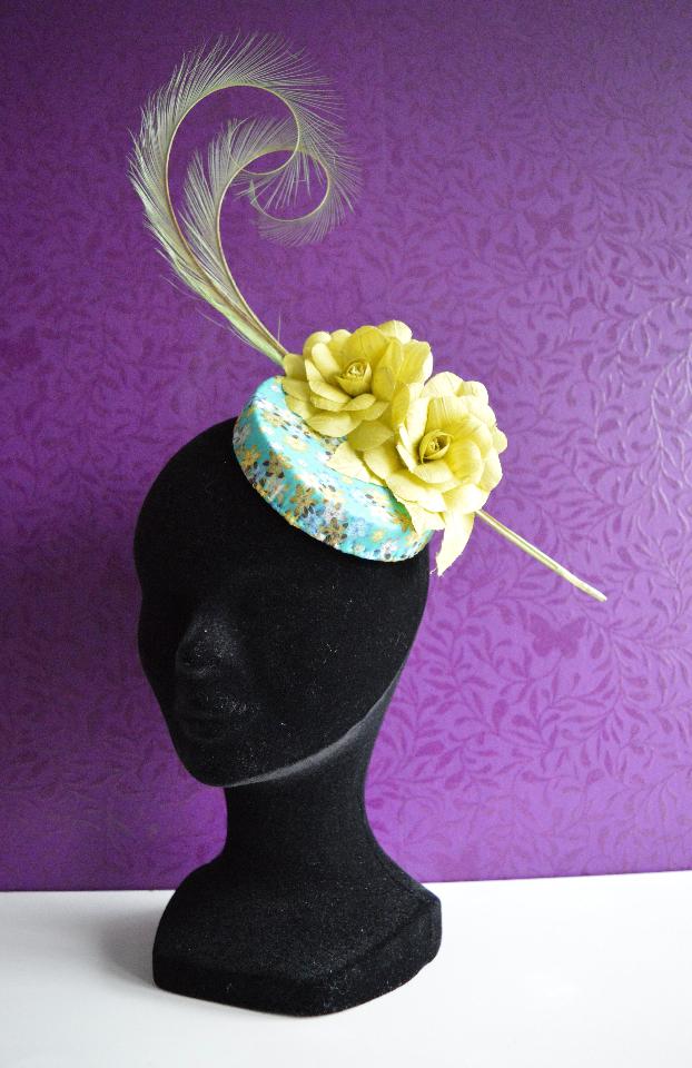 IMAGE - Handblocked fascinator covered in blue and yellow flower print fabirc. Decorated with curled feathers and two handmade flowers. Fixes with wigclips.