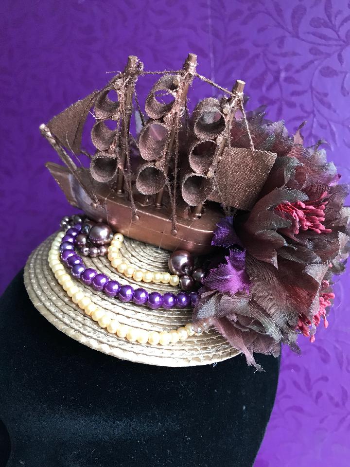 IMAGE - Light brown straw fascinator with copper boat, brown flowers and cream and purple pearls. Fixes to the hair with a comb.