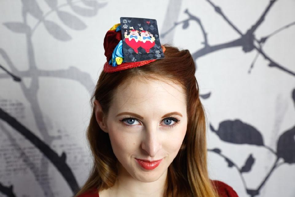 IMAGE - Red straw fascinator decorated with red, blue and yellow ribbon roses and playingcard featuring Tweedledee and Tweeldedum. Fixes to hair with a comb.