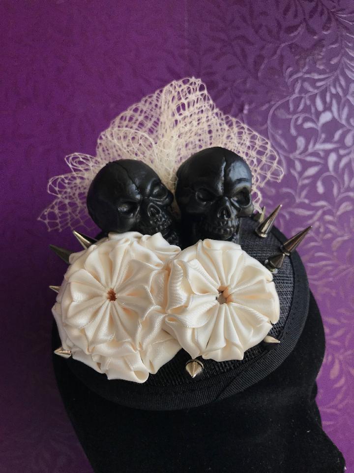 IMAGE - Black sinamay fascinator with black skulls, cream netting, cream ribbon ornaments and silver spikes. Fixes to the hair with a comb.