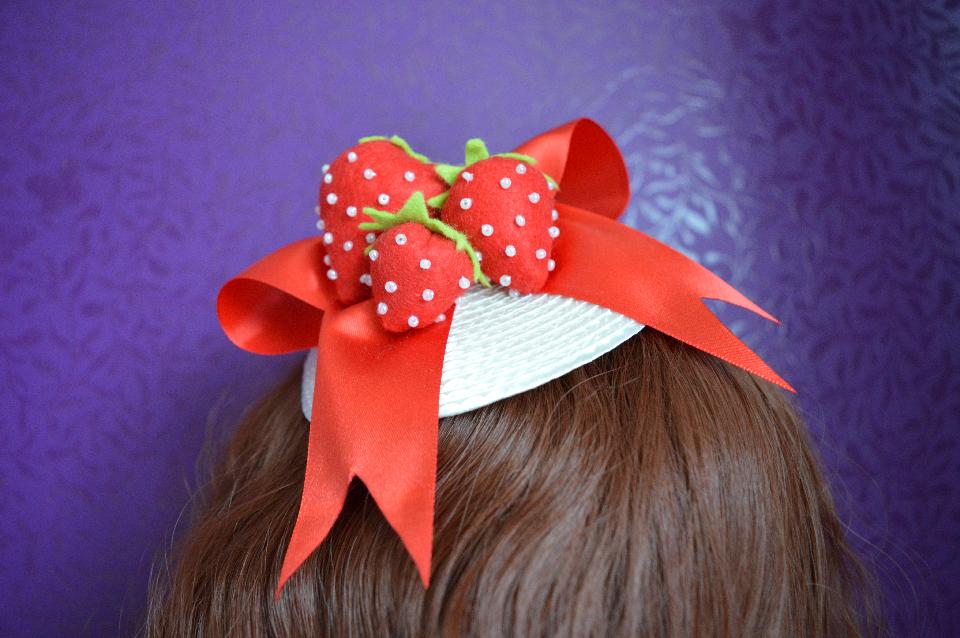 IMAGE - White fascinator with red satin bow and felt handmade strawberries. Fixes to hair with a comb.

Available from Loulou's Mechelen: https://www.facebook.com/Loulousmechelen/?fref=ts